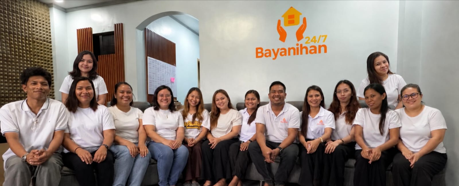 Bayanihan247 team gathered on a couch in the office with the company logo behind them